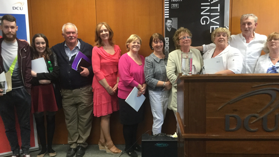 Shows a row of ten people standing against a wall