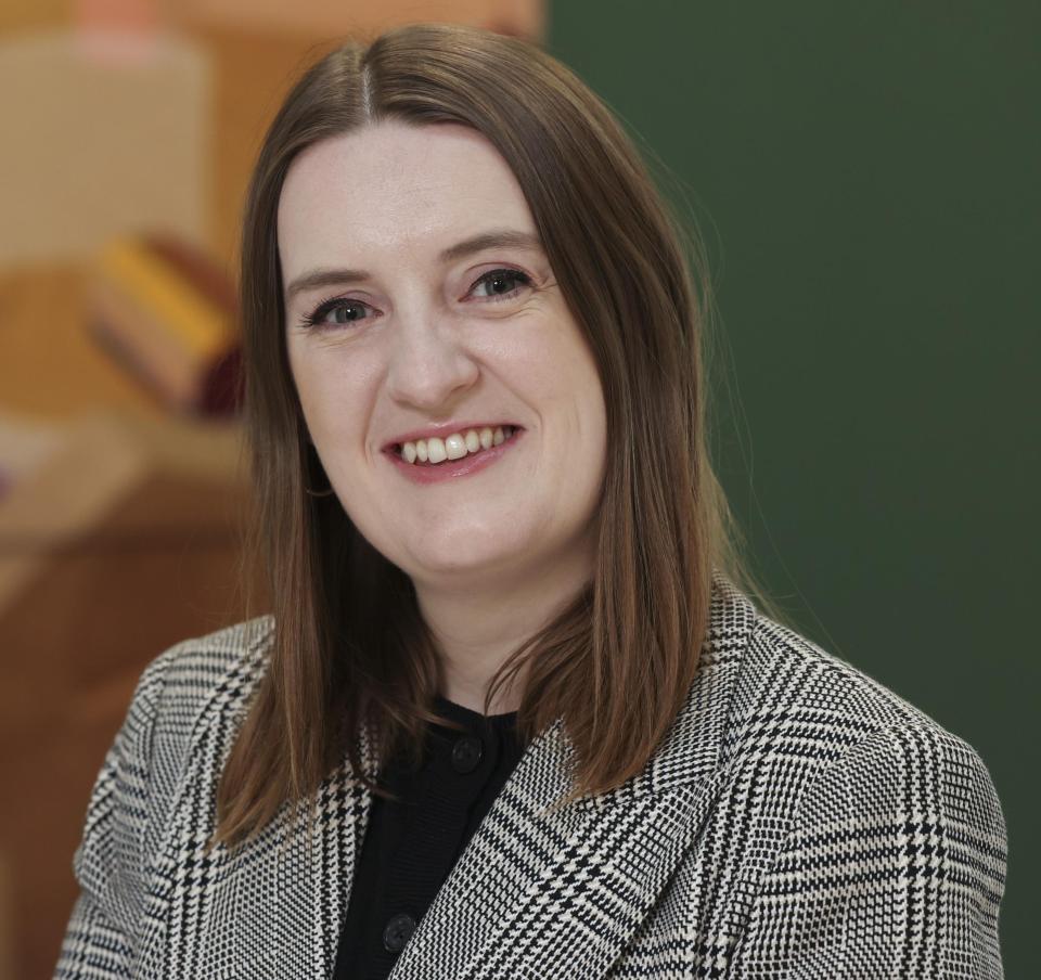 woman with brown hair in a black and white jacket against a green and orange backgroud 