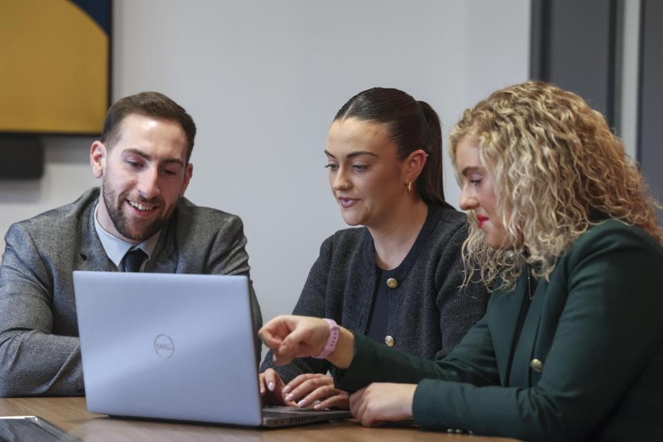three people sitting down looking at a laptop