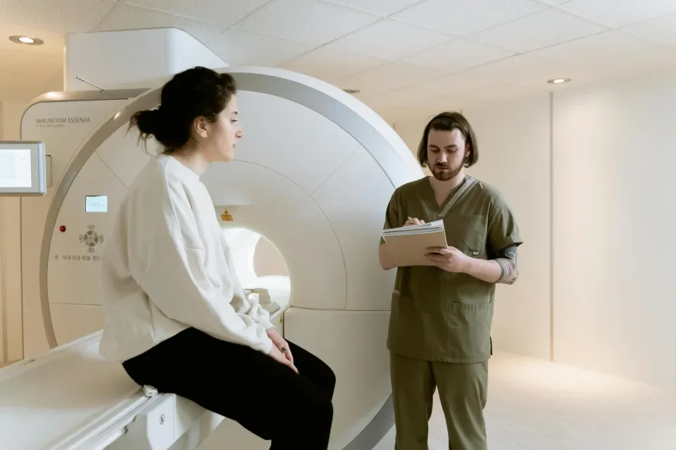 Woman sitting beside MRI machine with medic taking notes