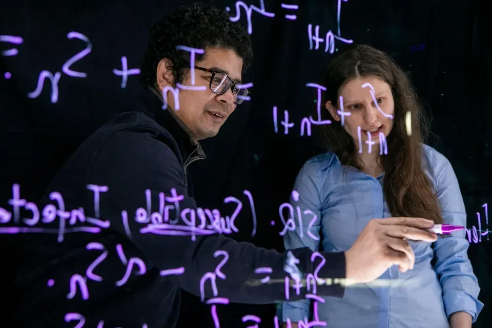 Two academics writing an equation on a board