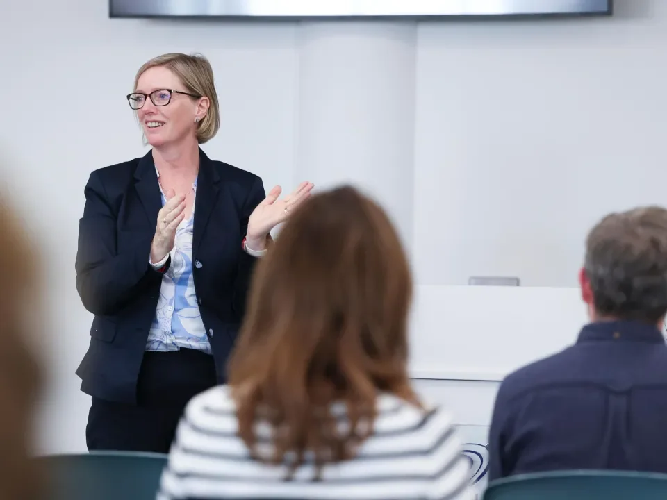 Shows woman speaking to crowd at conference style academic event