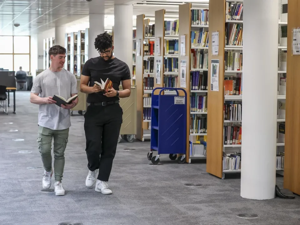 2 students walking and chatting near the book shleves on the first floor of O' Reilly library