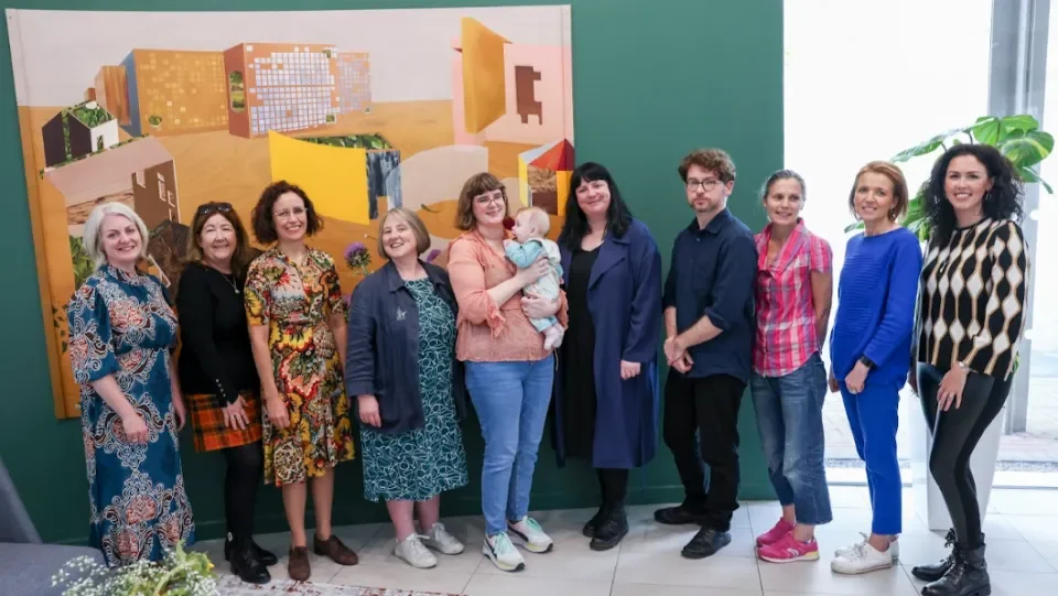 Group of 9 women and 1 man stand in front of large artwork
