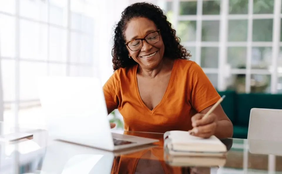 Older woman at computer writing on a notepad