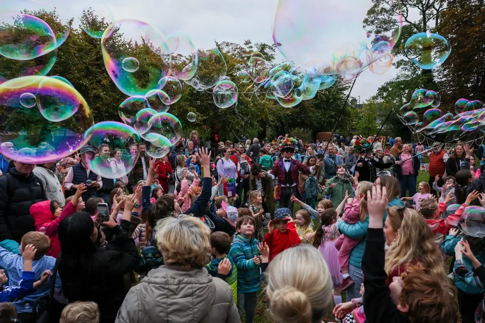 Children and adults gathered around large bubbles in a green field