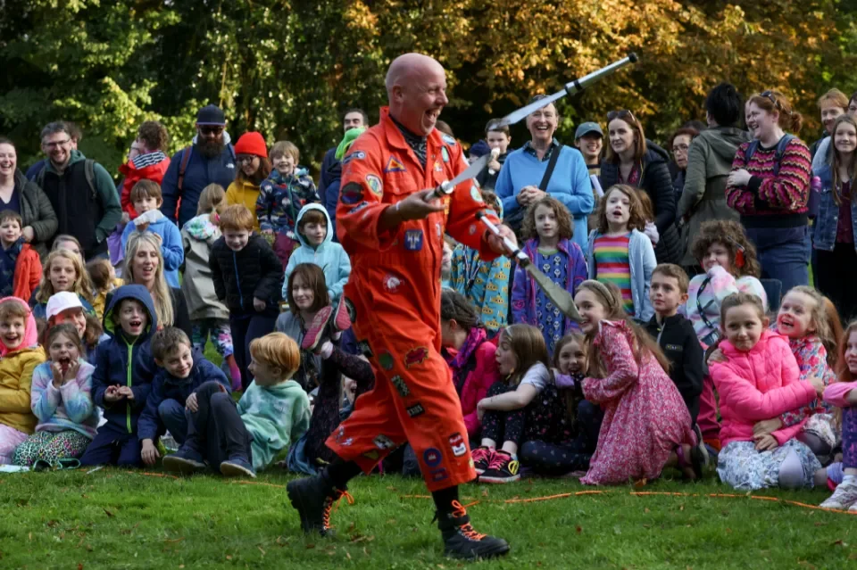 Performing circus artist juggles in front of children and adults who are smiling and laughing