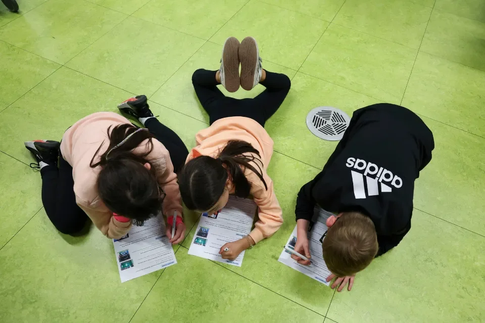 Three children lie on the floor colouring sheets of paper