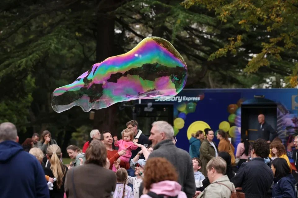 Large bubble floats in the sky above smiling crowd