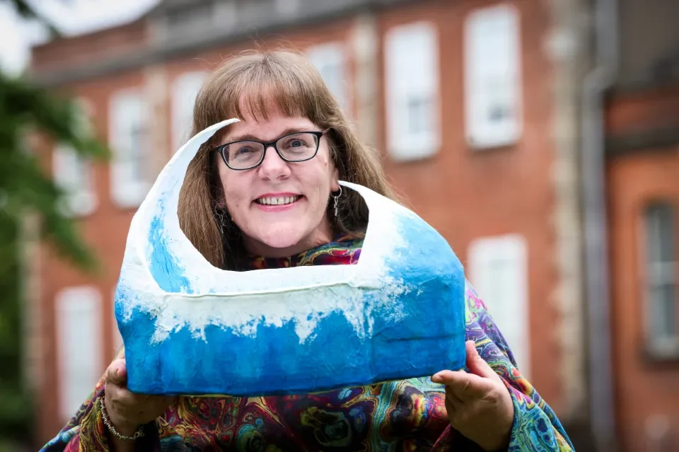 Woman with glasses smiling and holding blue wave art piece