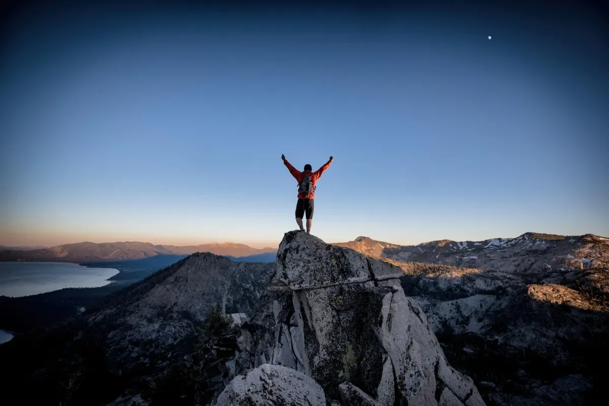 A man standing atop a mountain with his arms raised