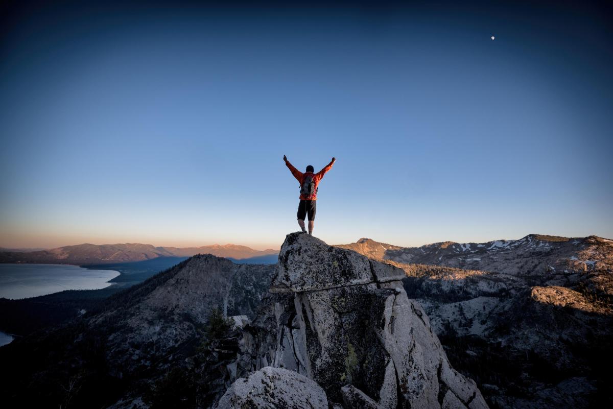 A man standing atop a mountain with his arms raised