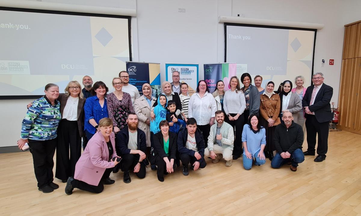 A group of people posing for a photo at a graduation event, standing and kneeling in front of banners.