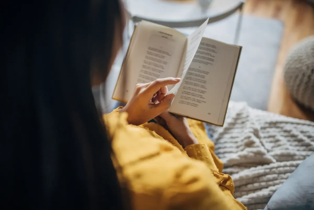A person reading a book, wearing a yellow garment.
