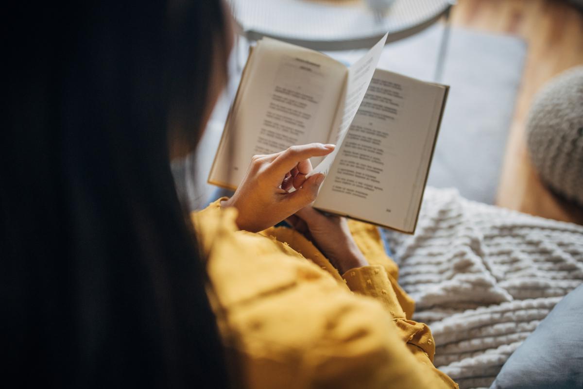 A person reading a book, wearing a yellow garment.