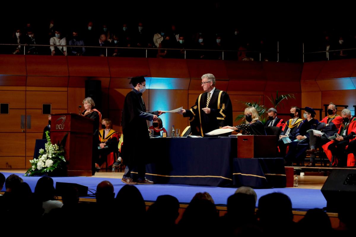 Graduate walks across the stage in O'Mahony Hall in the Helix