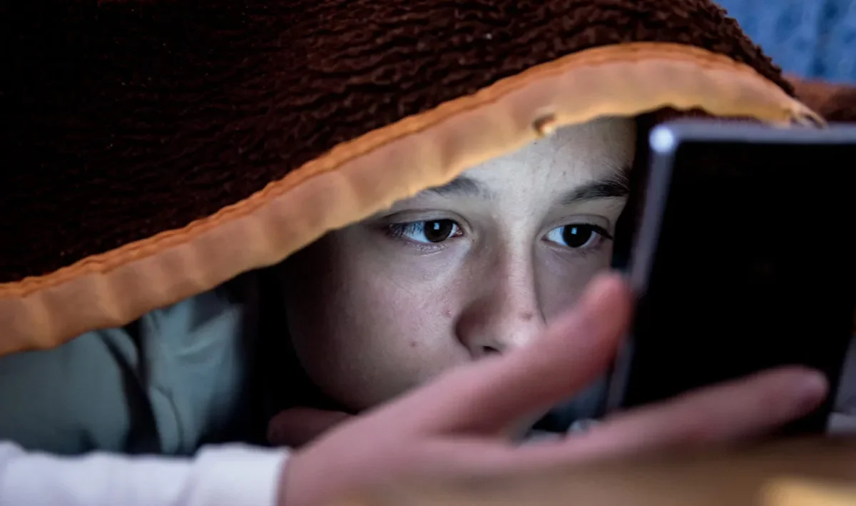 Child under blanket using mobile phone