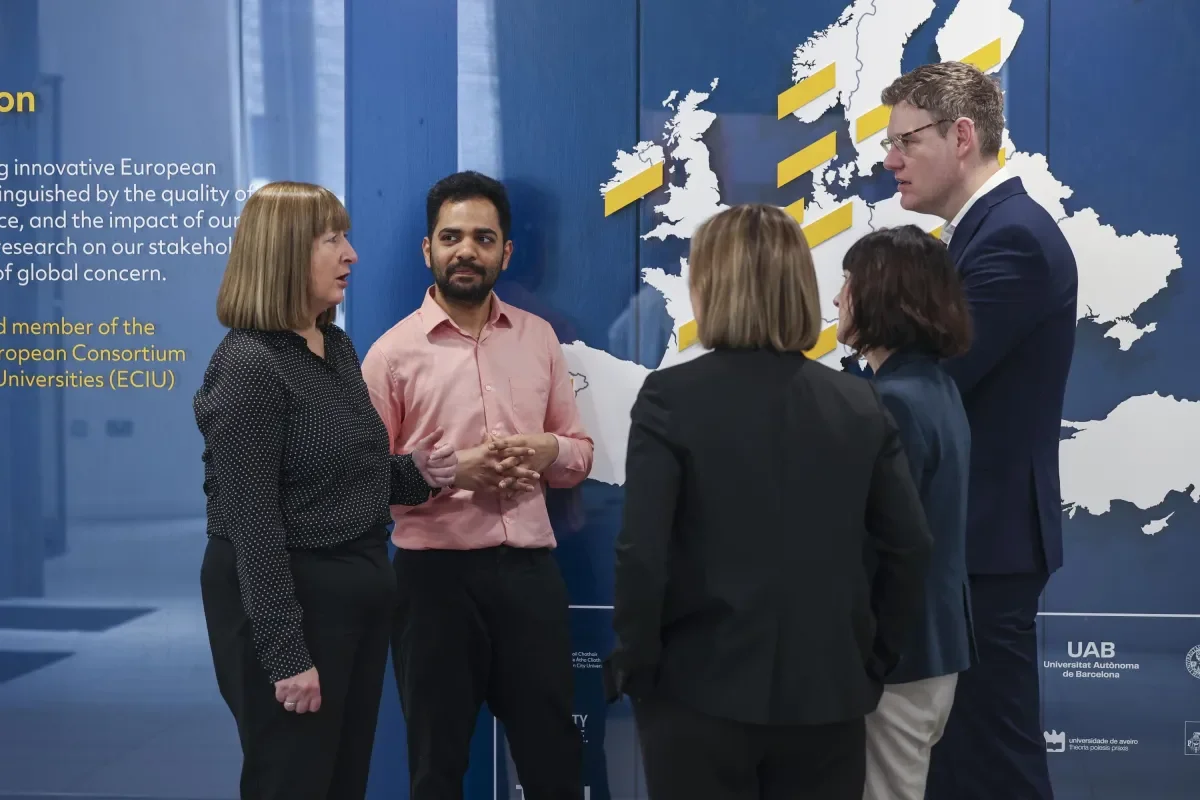 Five people in dialogue in front of a large banner with the world map on it