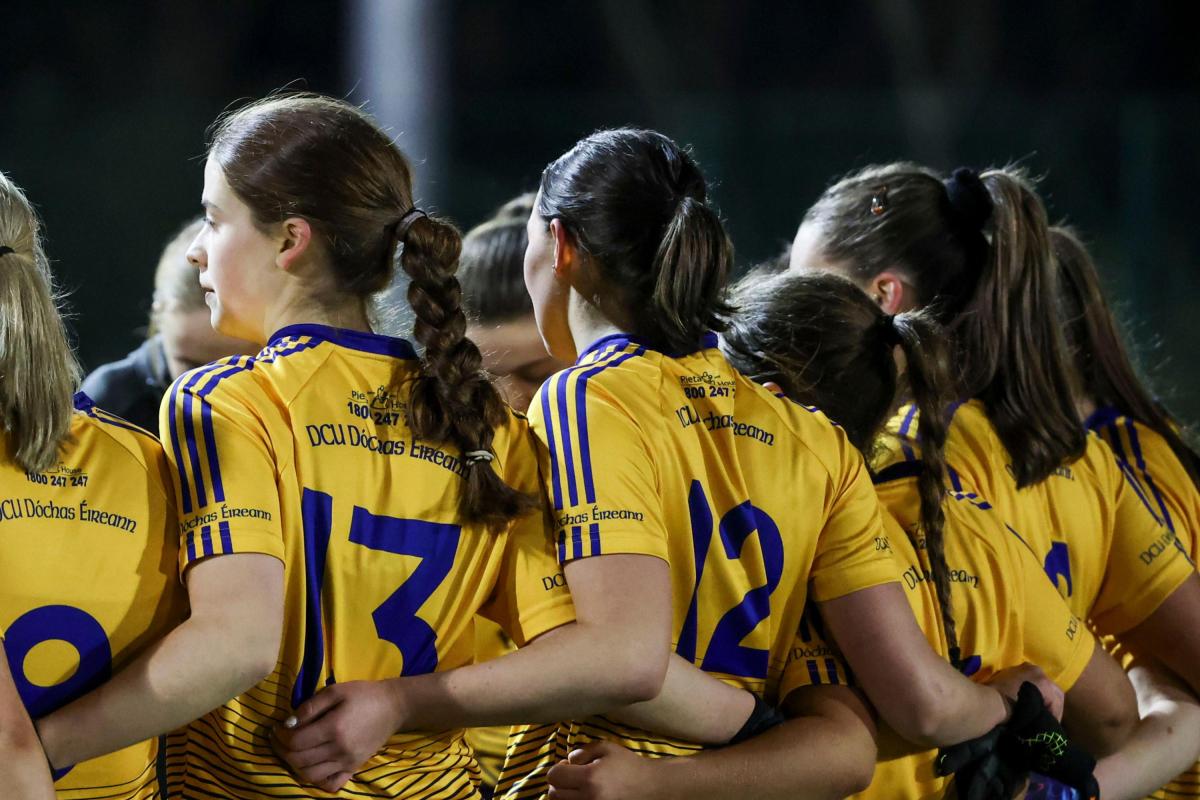 Shows DCU GAA players from behind, waist up with numbers visible on their jerseys