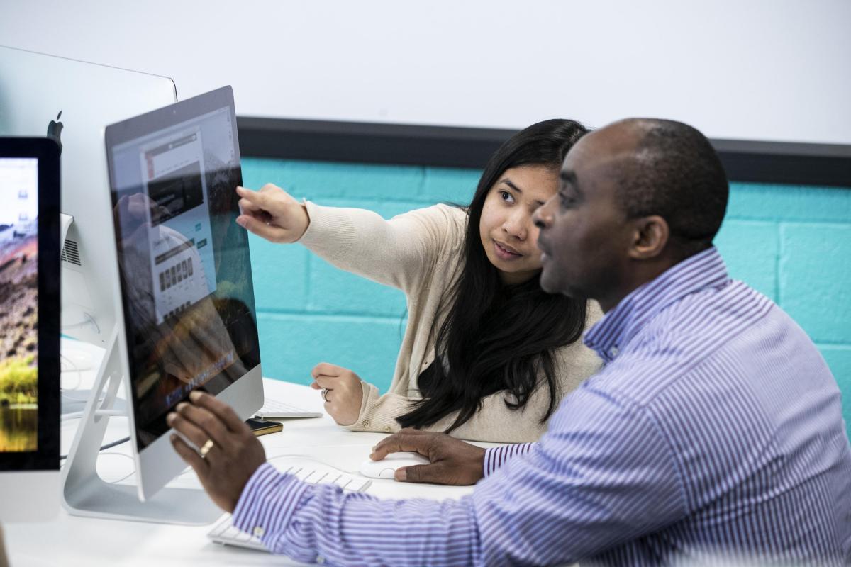 Picture of two students ( male and felmale) looking at a computer screen with the female student pointing at the screen