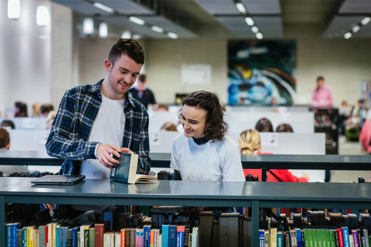 Two students reading a book in a library