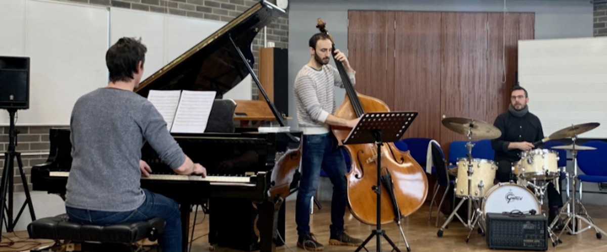 3 musicians playing - one plays piano, one plays double bass and one plays drums