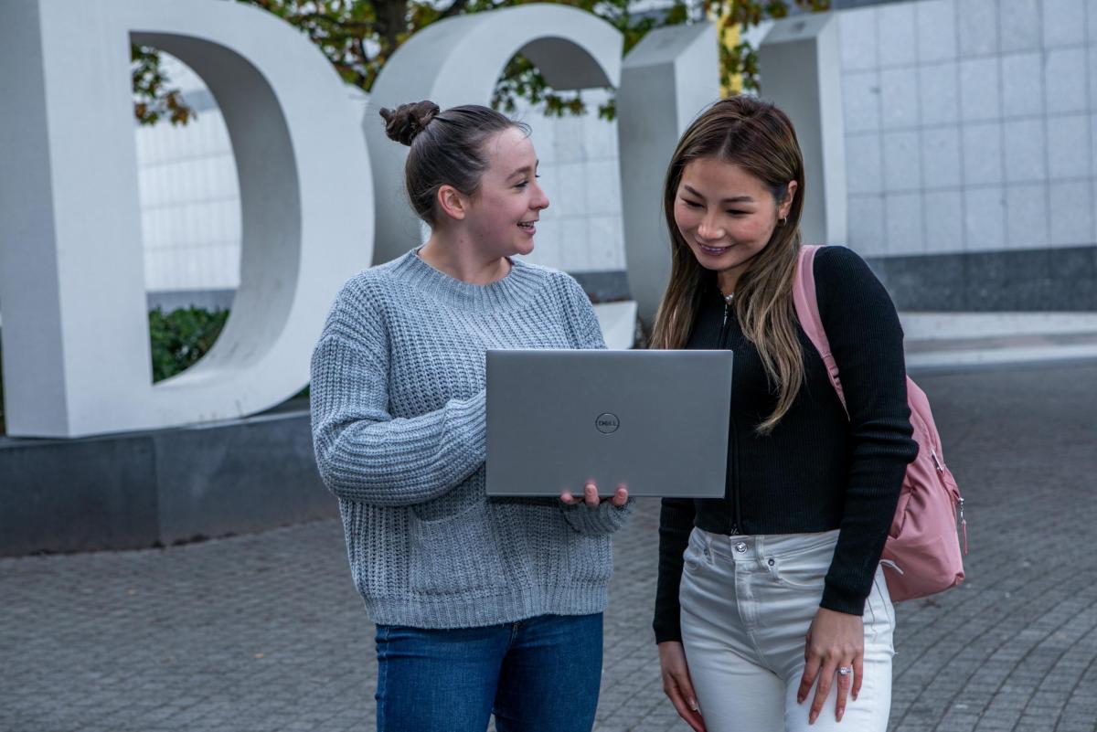 Students stand and use a laptop