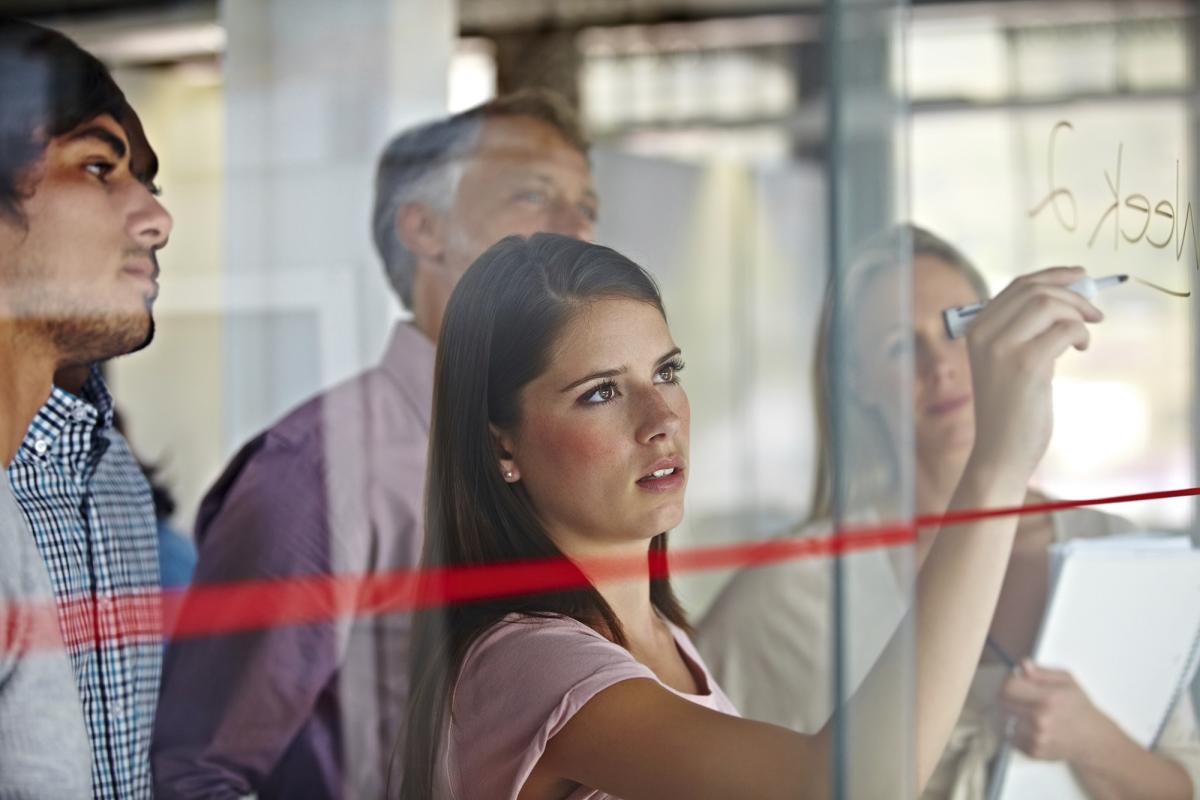 Image of female writing on a board and a group of colleagues watching