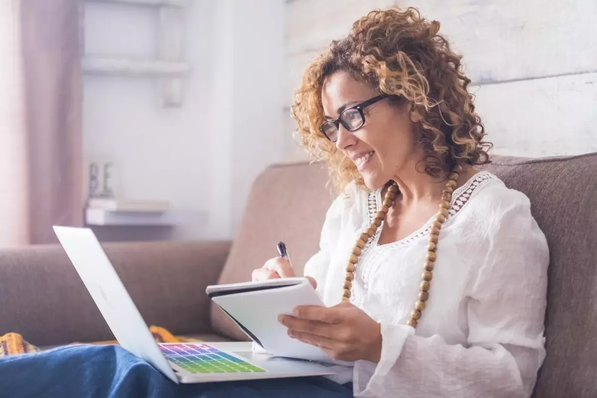 Woman writes notes while looking at laptop