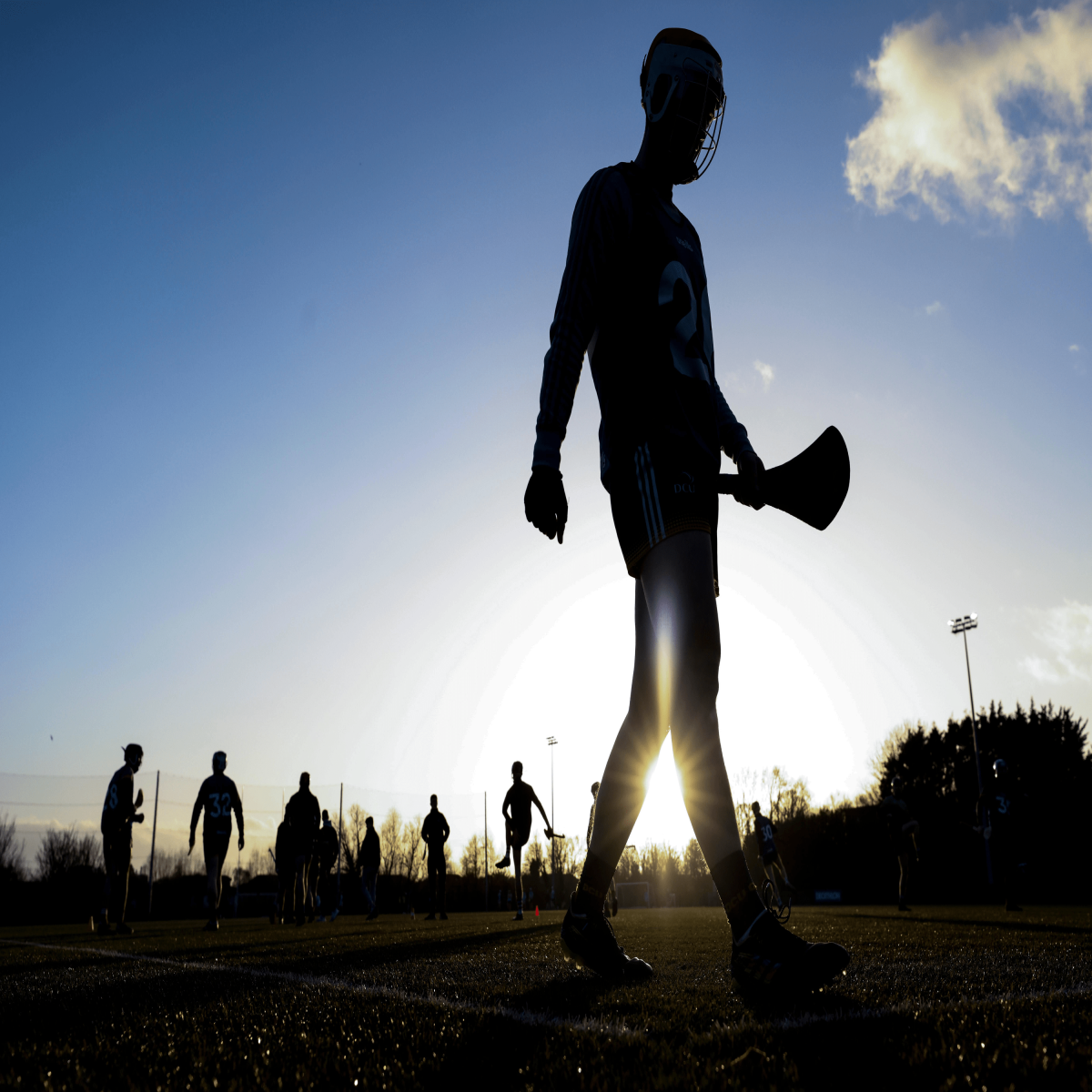 A hurler in shadow with a team training behind them.