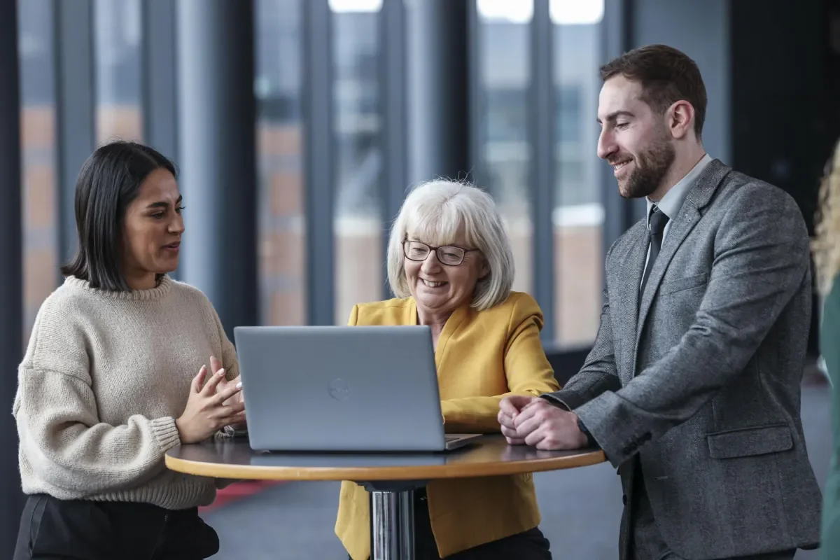 3 staff members standing looking at laptop on high table