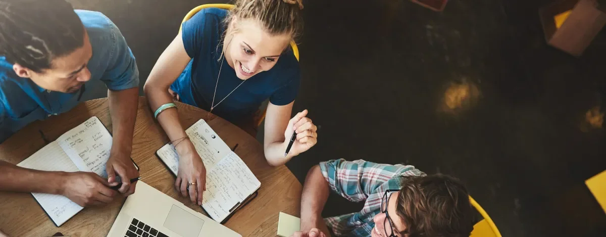 3 people at a table with notebooks and a laptop