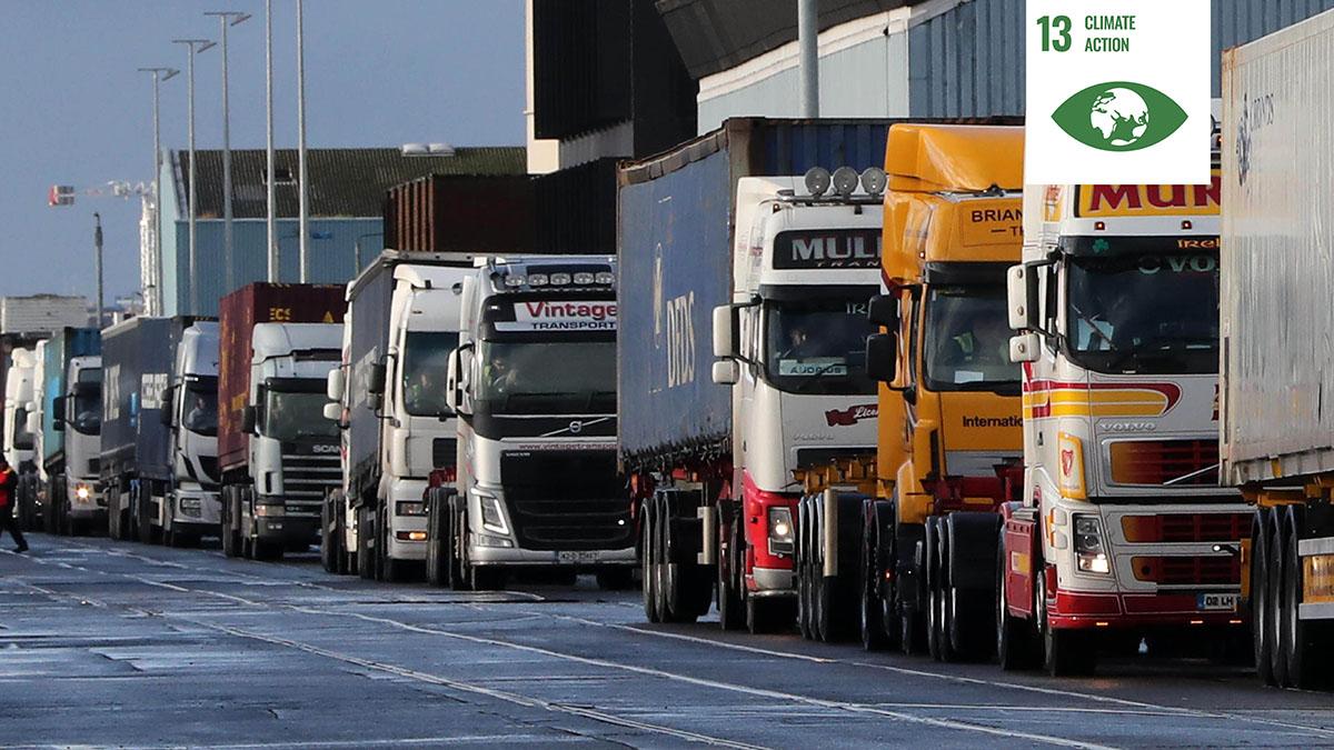 Shows a line of heavy goods vehicles at Dublin Port with a white icon signifying UN Sustainable Development Goal thirteen
