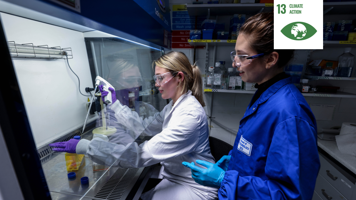 Shows two women working in a lab wearing protective eyewear and clothing with a white icon signifying thirteen