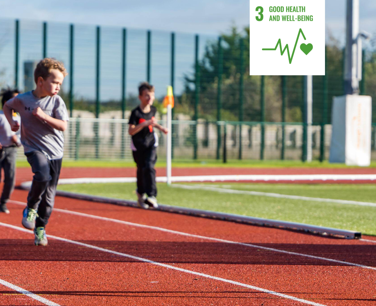 Shows young children competing in a race on a running track with a white icon signifying UN Sustainable Development Goal three