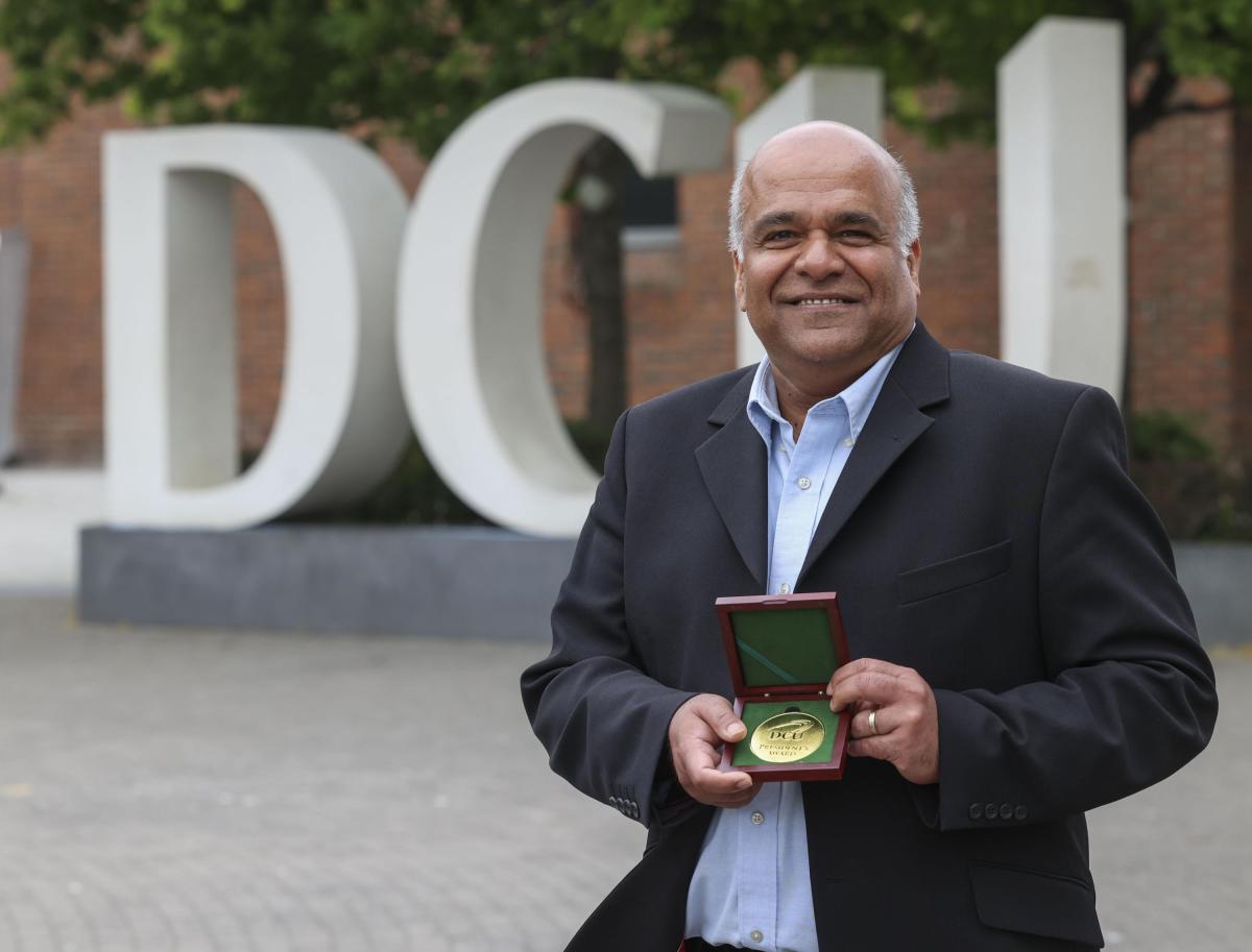 Shows Dr Prince Anandarajah in front of the DCU logo on campus after receiving a research award