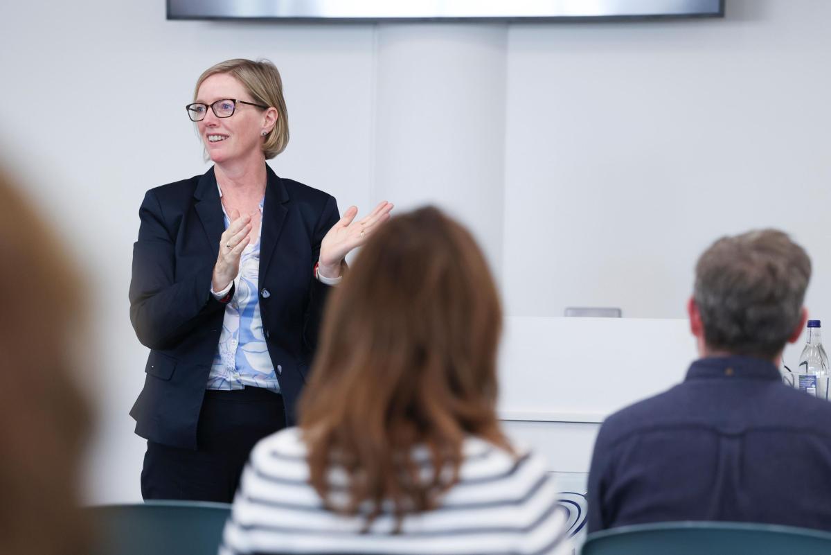 Shows woman speaking to crowd at conference style academic event