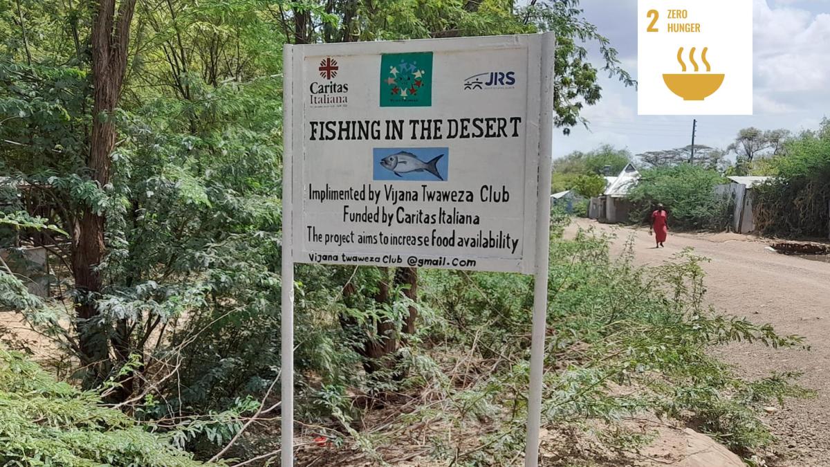 Shows signage for community project in Kakuma refugee camp in Kenya reading 'Fishing in the Desert'