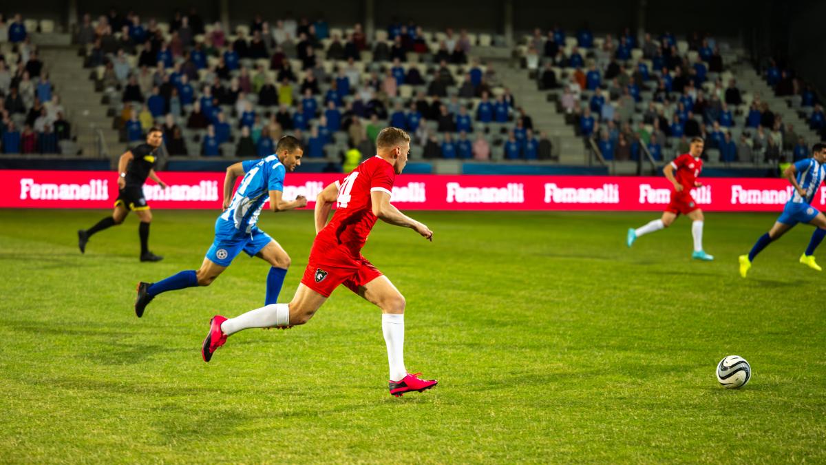 Shows footballer dribbling into opposition's half, members of the other team in the background