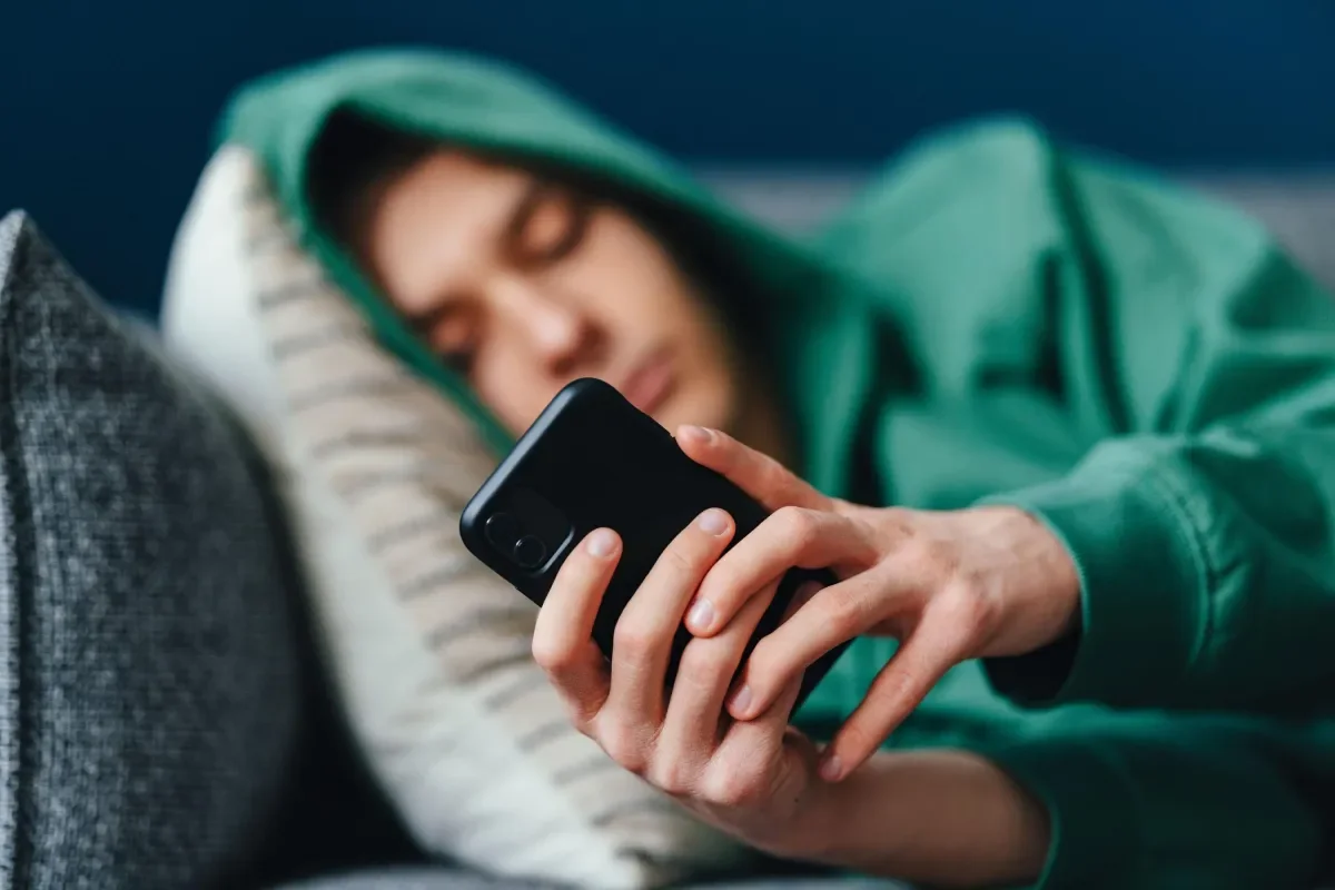 Shows teenage boy lying on couch using smart phone