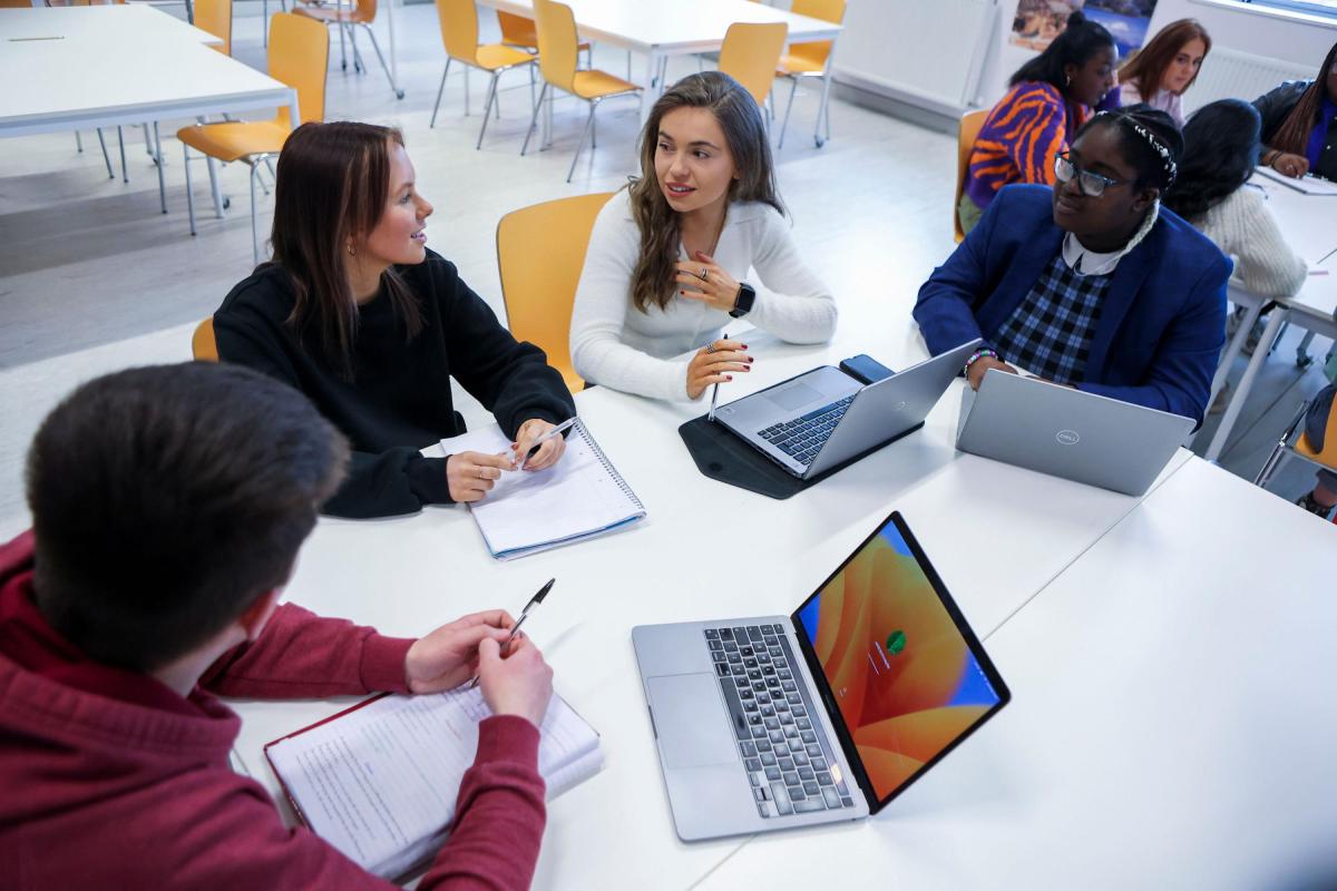 Students chatting around a table with laptops in front of them