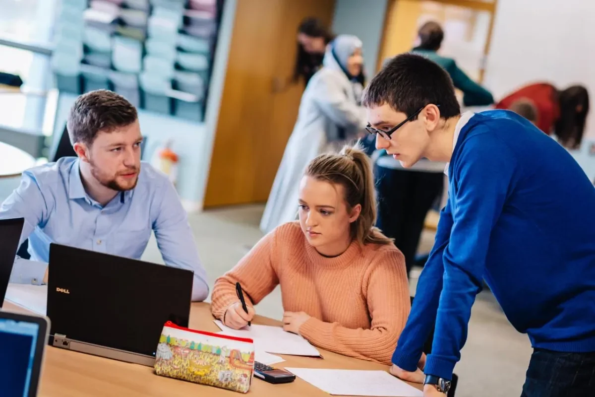Three students at a desk collaborating on an iPad