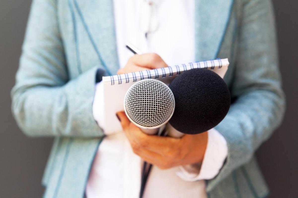 Student holding a microphone and writing on a notepad 