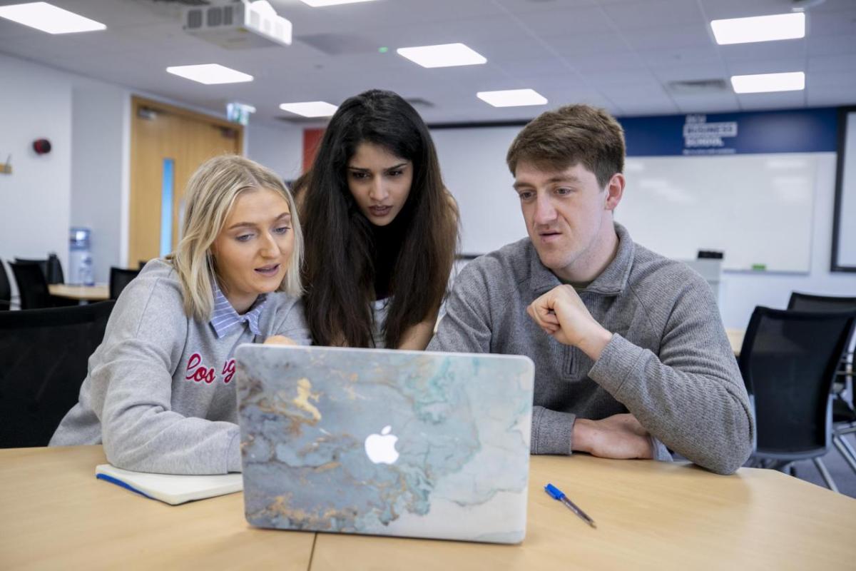 Three students collaborating at a desk using a laptop