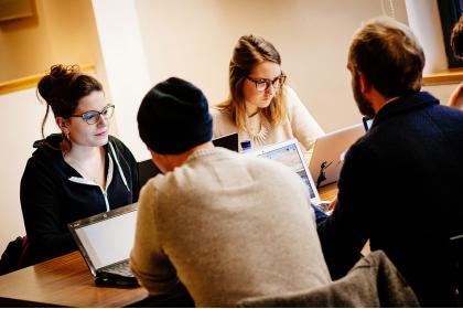 Four students collaborating at a desk using laptops