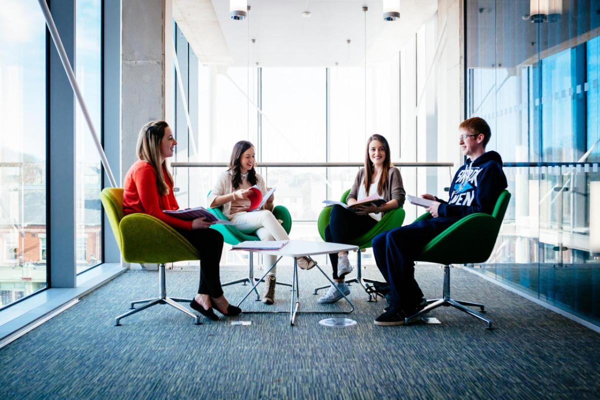 four students sitting at a desk chatting