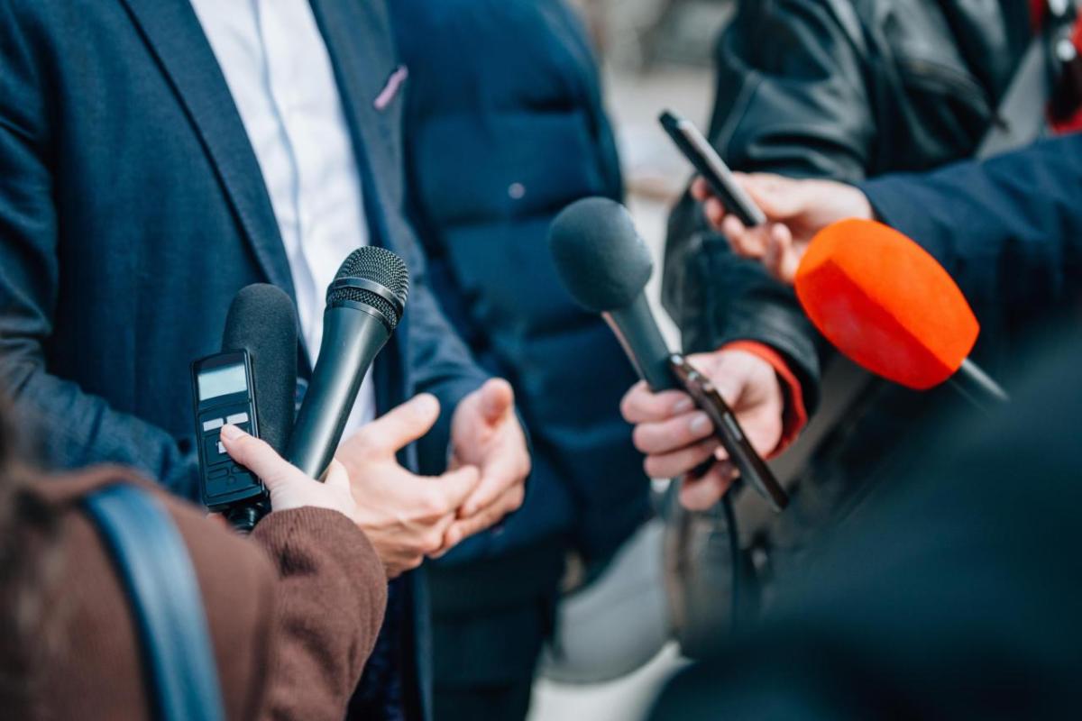 Microphones directed at three people communicating to the press