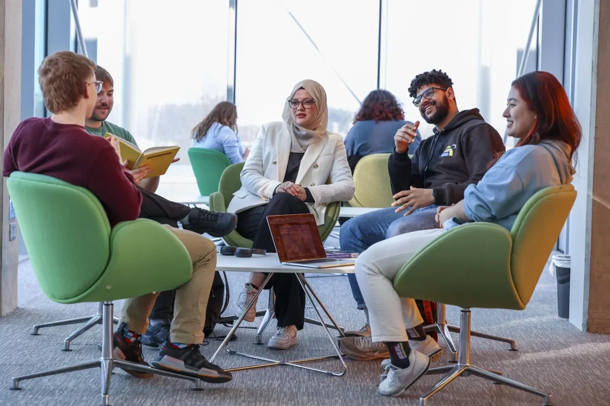 a group of 5 students sitting on comfortable, colourful chairs in a sunny part of Cregan library. Thye are smiling and chatting