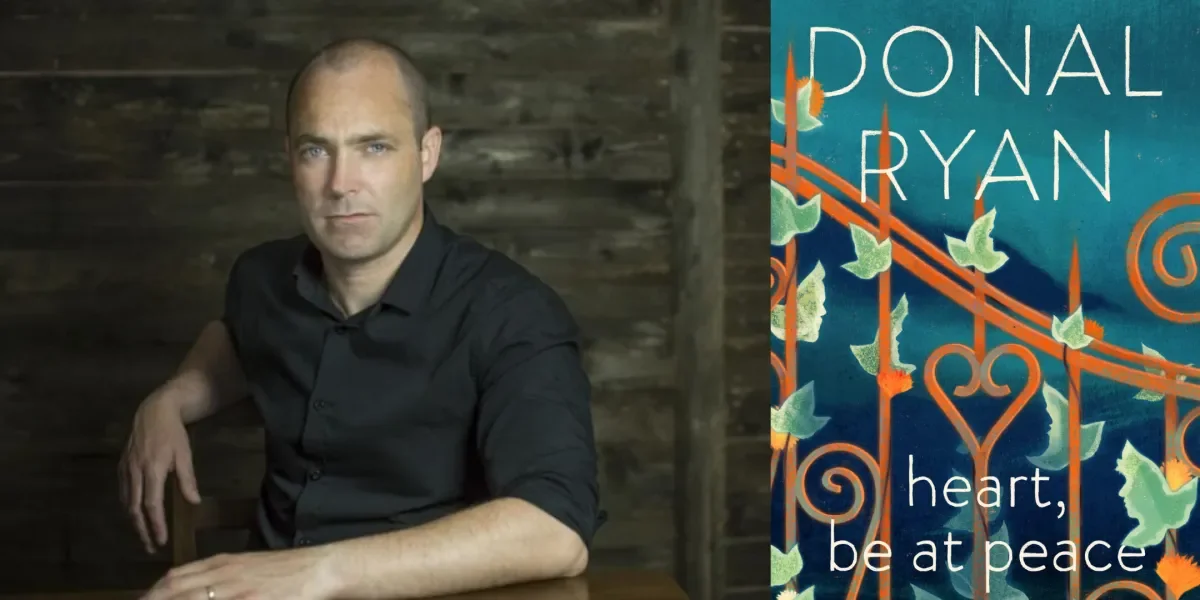 Author Dolan Ryan, man with shaved head sits at a table with a black background.