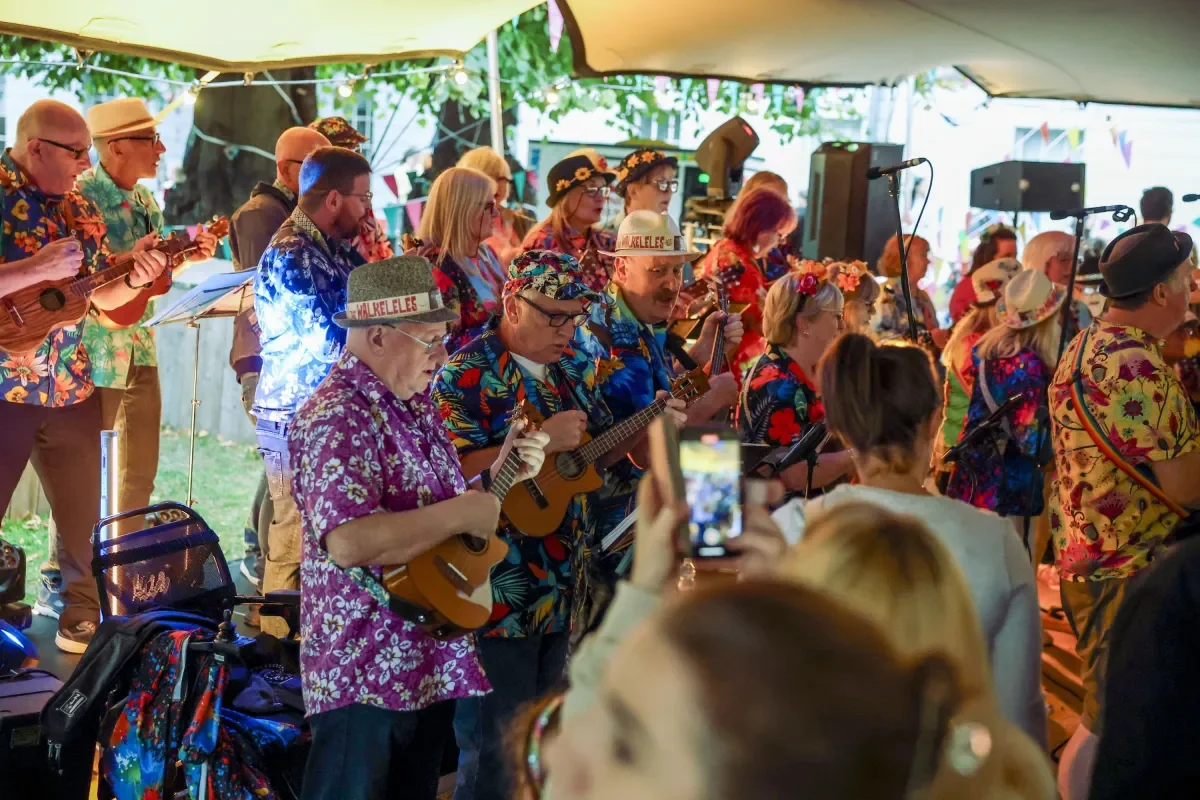 Group of people singing, playing ukuleles and wearing bright coloured shirts  